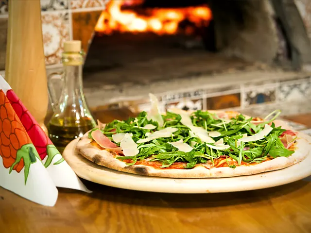 Pizza z szynką dojrzewającą, rukolą i parmezanem przed rozgrzanym piecem